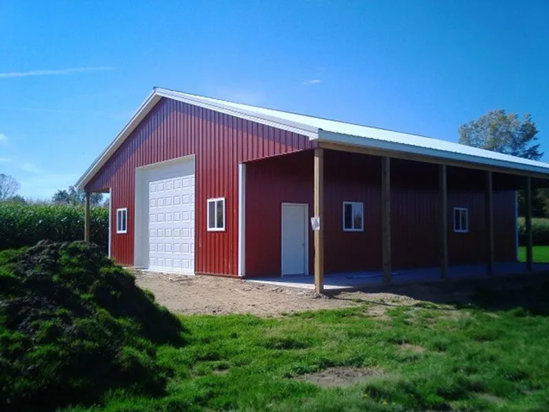 A red metal barn with white trim, one large garage door, and an attached open-sided covered area on a grassy plot.