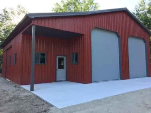 Red metal building with two large gray garage doors, three windows, and a white entry door on a concrete pad.