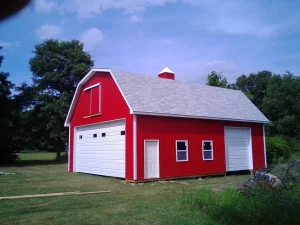 A red barn-style garage with white trim, two garage doors, three windows, and a side door, set on grass.