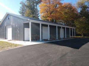 A gray metal building with a covered walkway and several doors, surrounded by trees with autumn foliage.